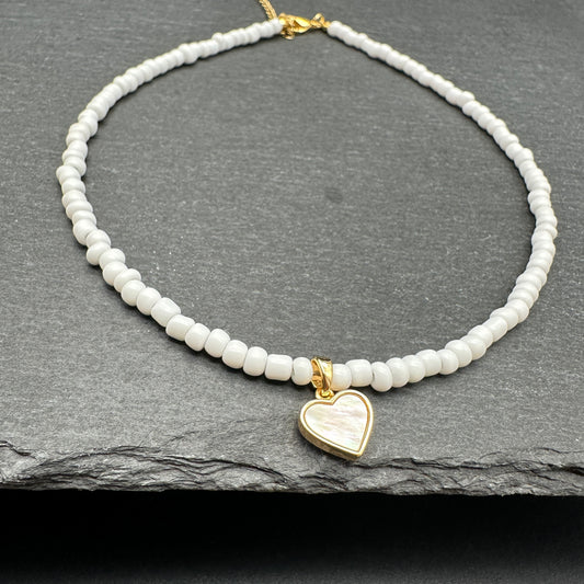 Necklace with white beaded chain and gold mother of pearl heart pendant on a dark surface
