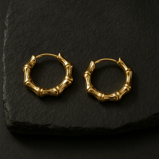 Pair of 18 K gold-plated bamboo-style mini hoop earrings on dark granite with top-right lighting