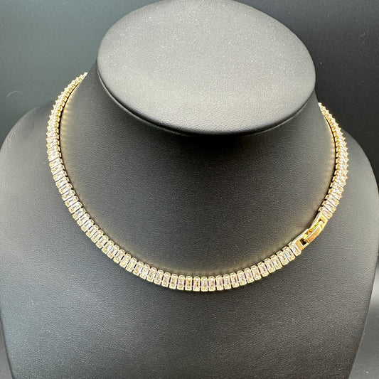 Close-up view of baguette-cut cubic zirconia stones in an 18K gold-plated tennis necklace, secure box clasp.