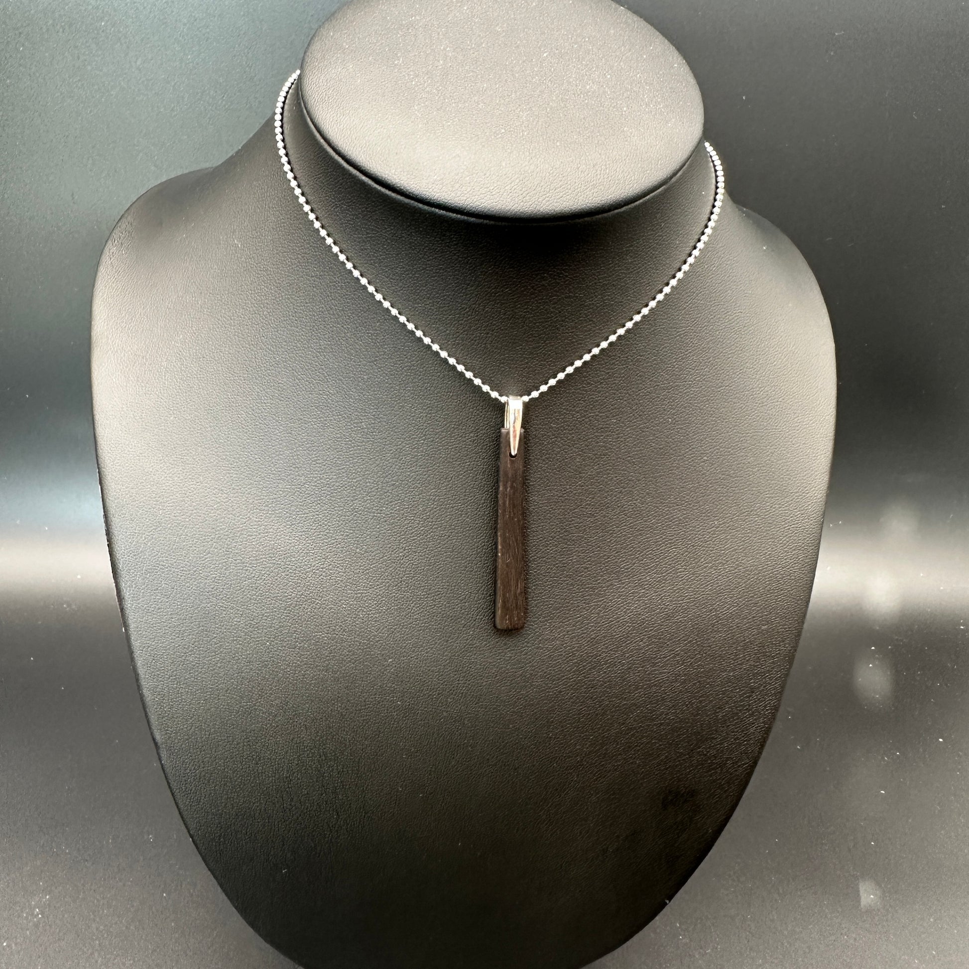 Necklace with a vertical ebony pendant on a mannequin bust against a neutral background