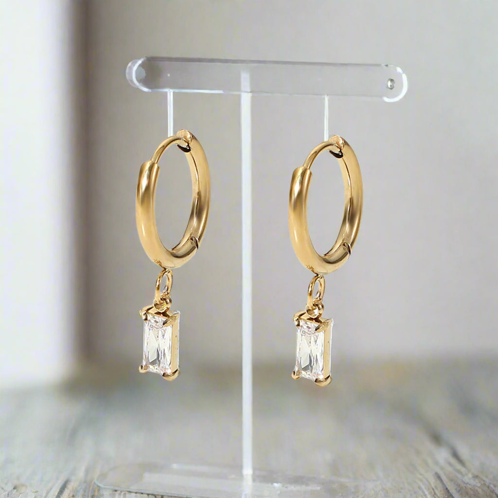 A gold-plated huggie hoop earring featuring an emerald-cut clear cubic zirconia drop