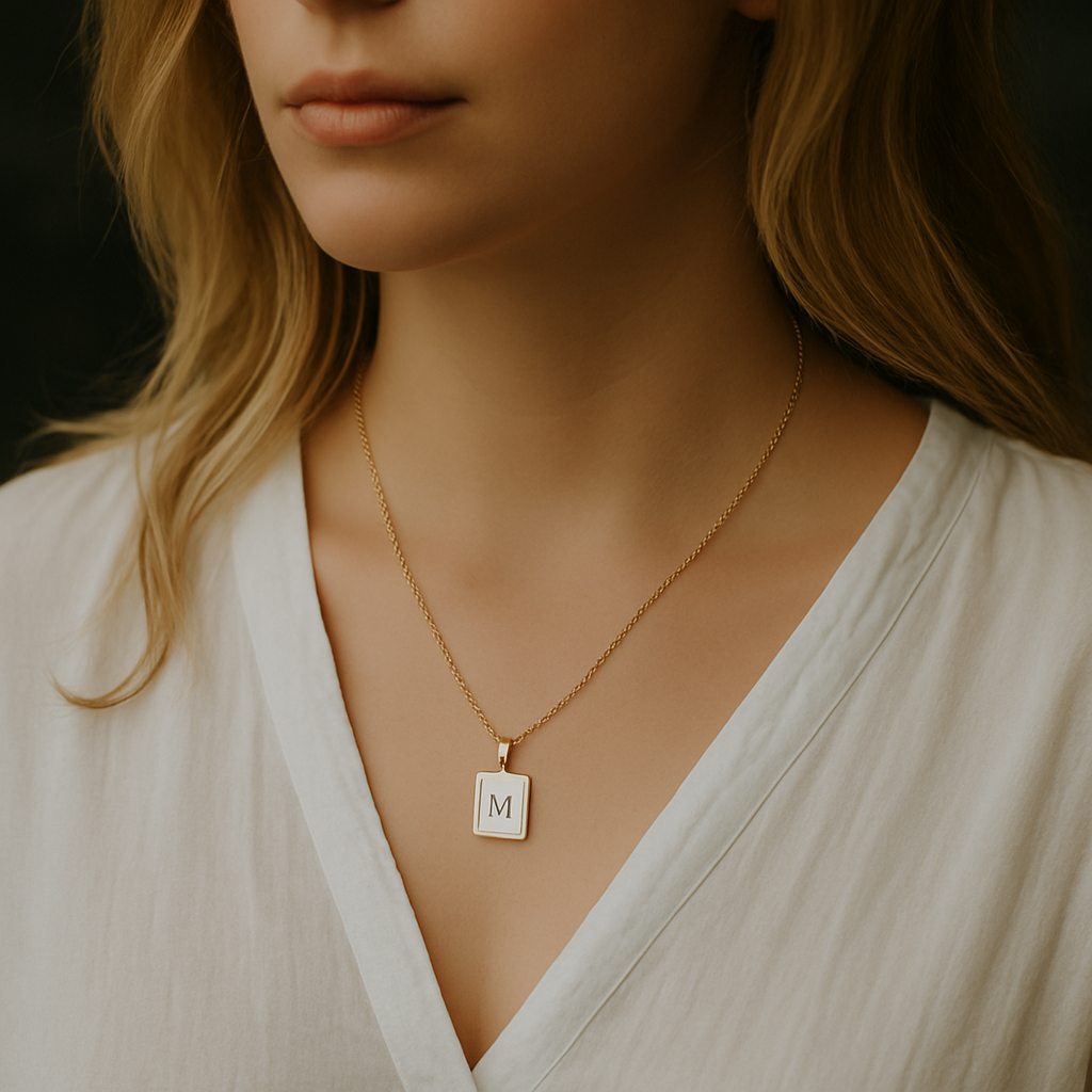 Woman wearing a gold necklace with a square pendant featuring the letter 'M' against a dark background.