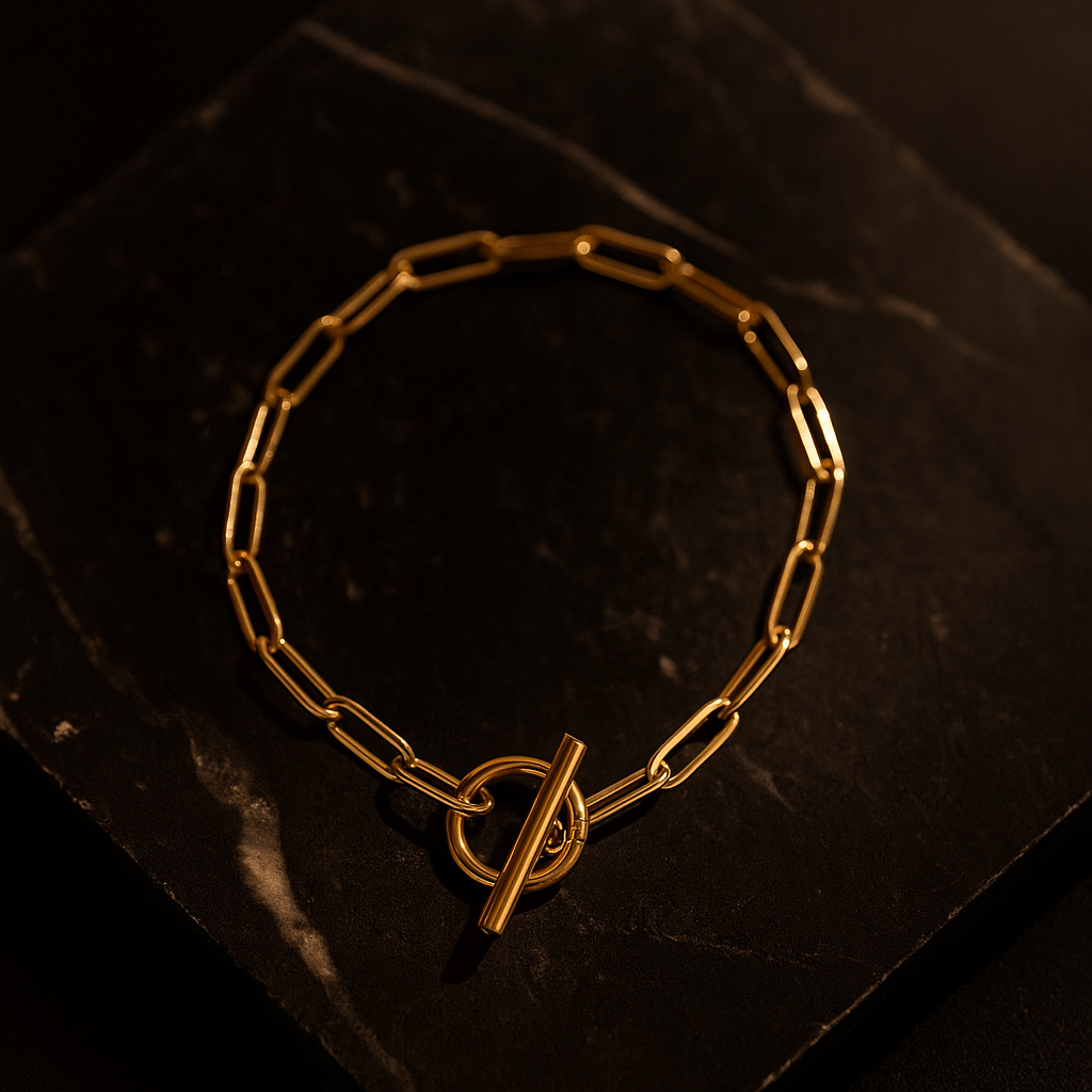 gold paper clip bracelet with toggle chain featured on a piece of dark granite. 