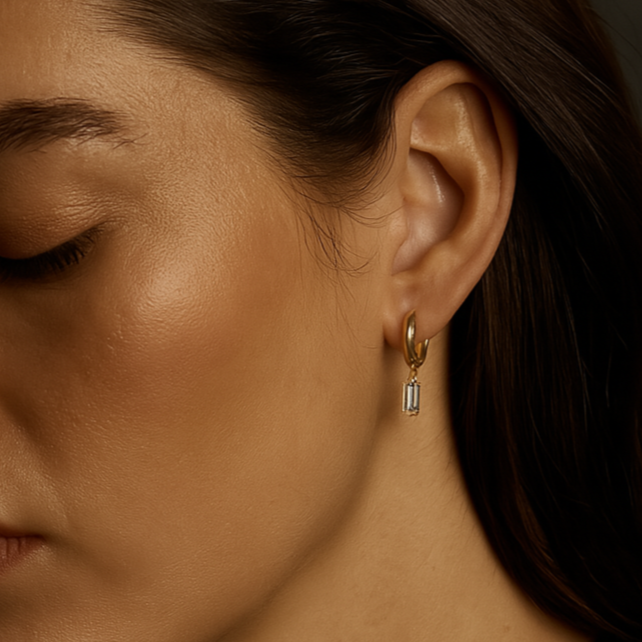 A gold-plated huggie hoop earring featuring an emerald-cut clear cubic zirconia drop